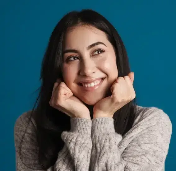 Smiling woman in a gray sweater resting chin on clasped hands, looking sideways.
