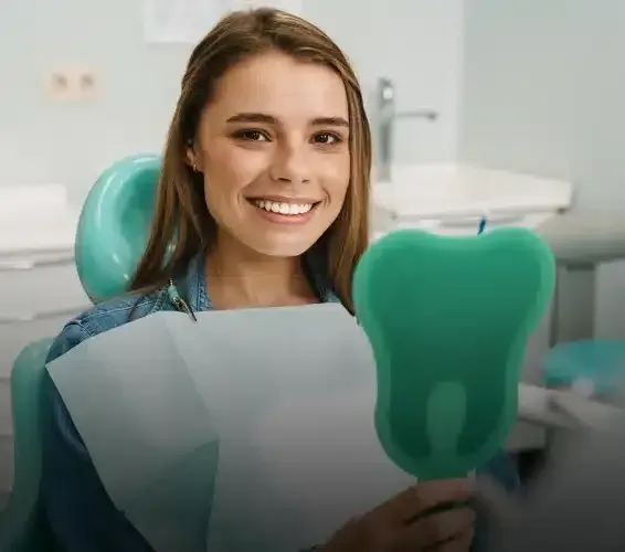 Smiling woman in dental chair holding a tooth-shaped mirror fan.