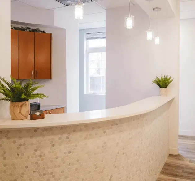 Curved tiled reception desk with potted ferns, pendant lights, and wooden cabinets.