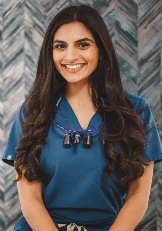 Smiling woman in teal scrubs wearing surgical loupes around her neck.